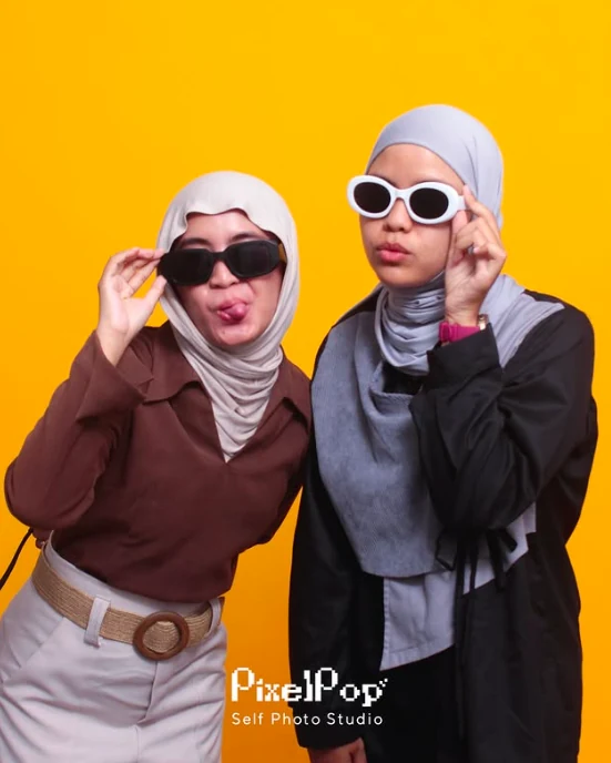 Dua orang berpose di studio PixelPop dengan latar kuning