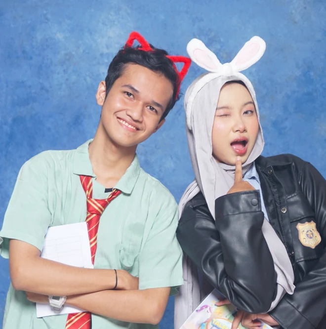 Dua orang berpose di studio PixelPop dengan latar biru